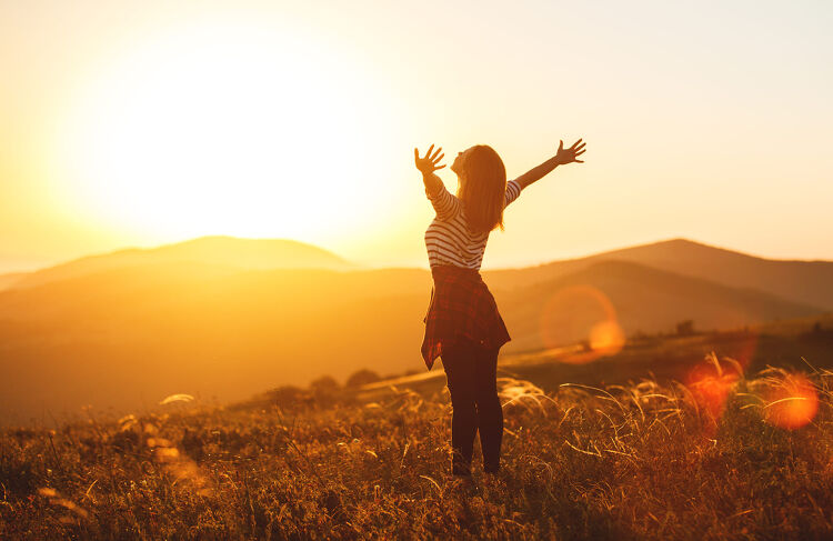 Woman standing in a field with arms raised toward the sunset